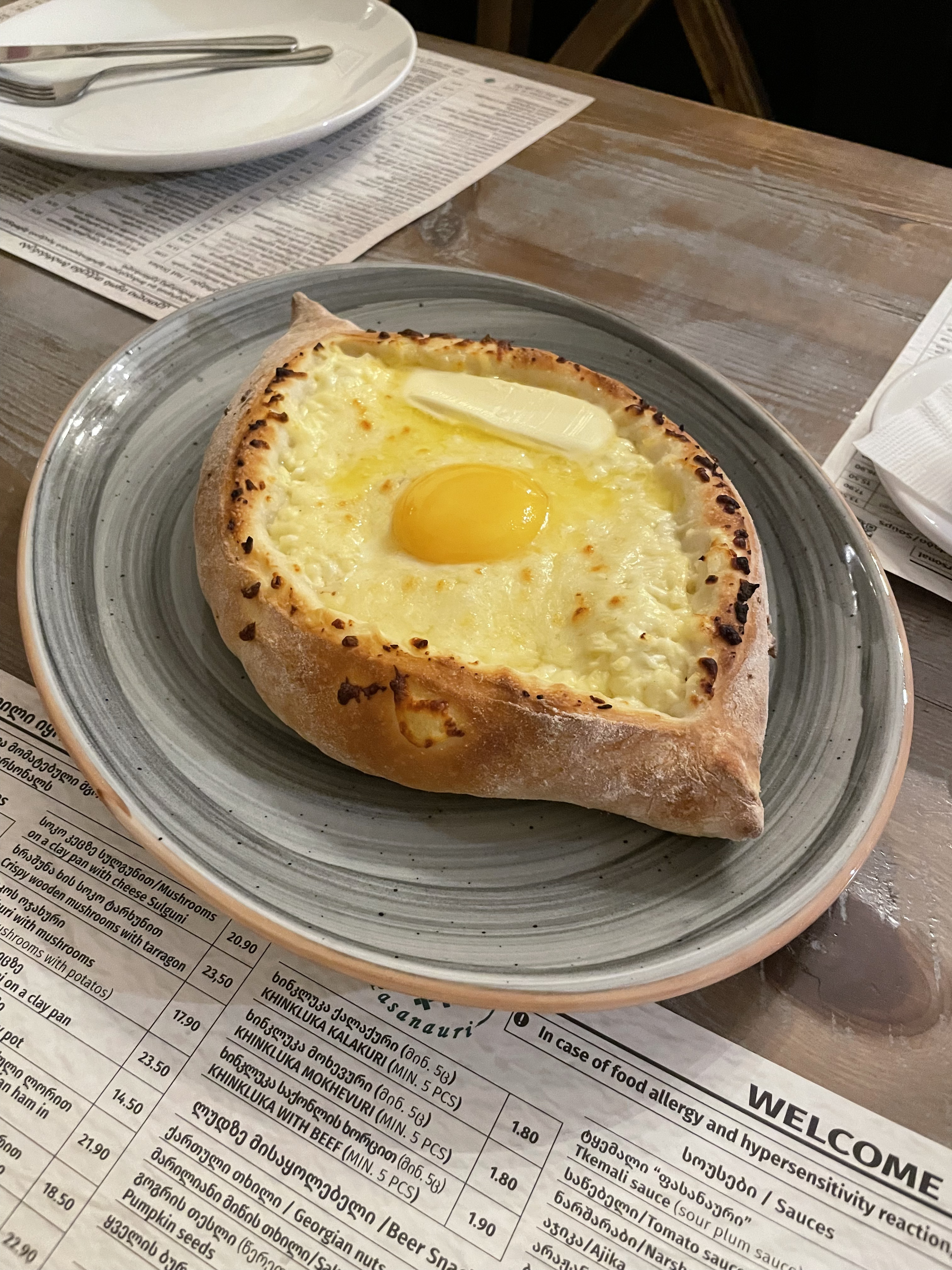 Аджарский хачапури с яйцом и маслом Аджарский хачапури с сыром, желтком и кусочком сливочного масла на серой тарелке